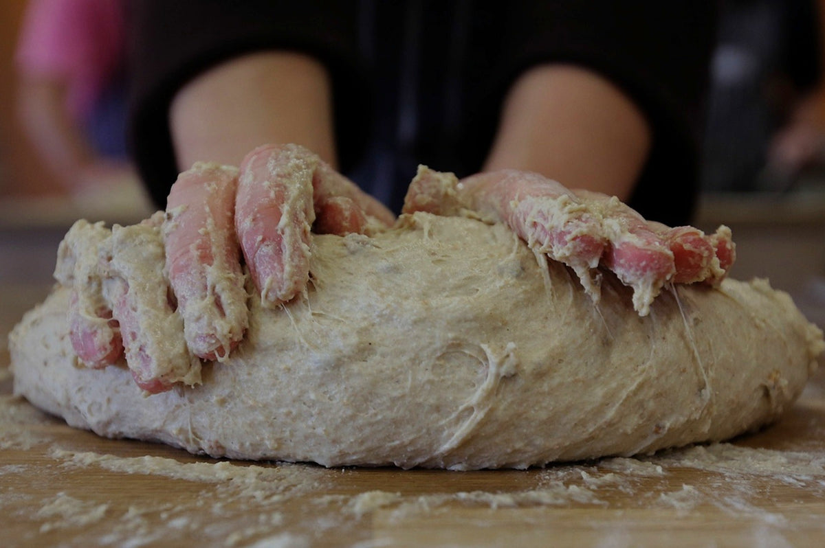 Close-up of two hands working a large mass of sticky bread dough on a floured wooden table