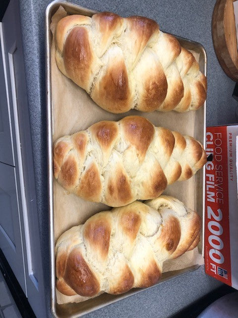 Three golden-baked braided challah loaves cooling on parchment in a sheet pan