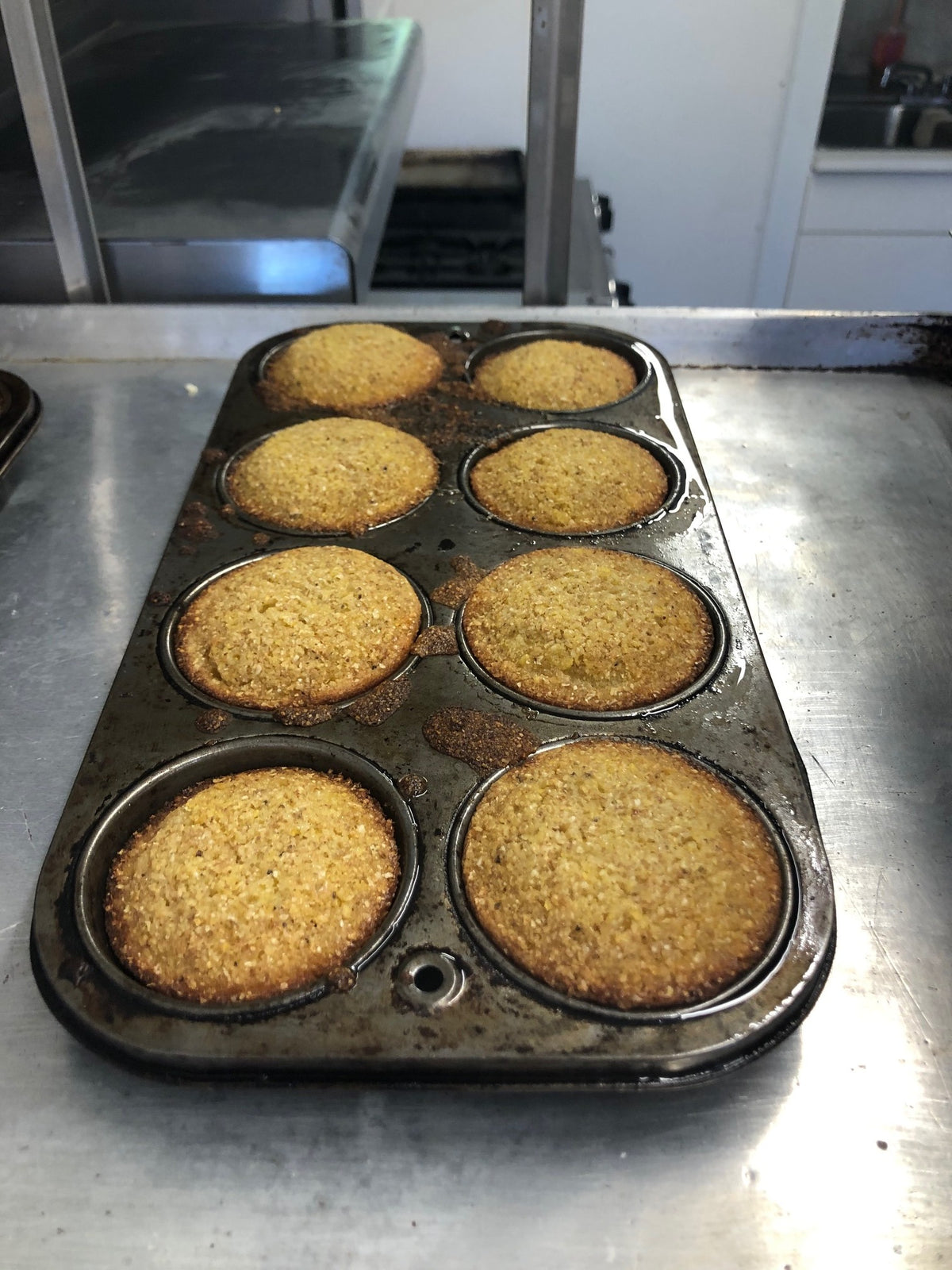 Eight baked cornmeal muffins in a well-seasoned steel muffin tin, fresh from the oven
