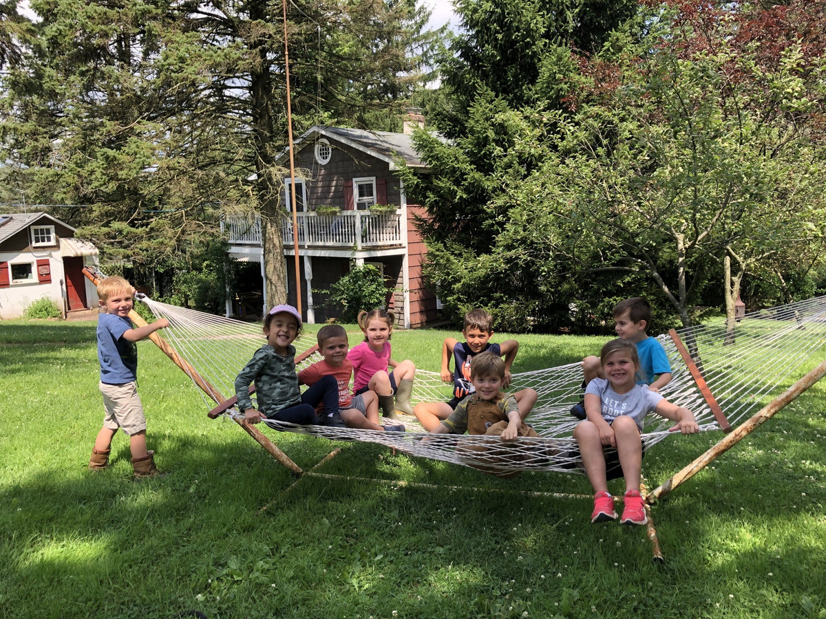 Eight young children sitting together on a rope hammock on the farm lawn, the shingled farmhouse behind them