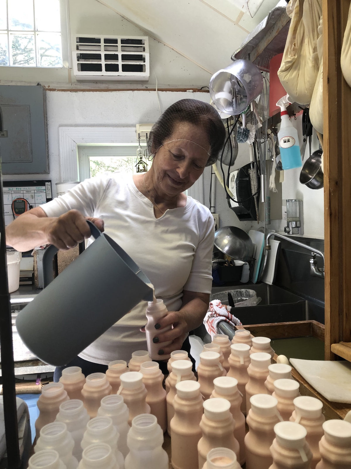 An adult in a hairnet pouring milk into bottles in the processing room
