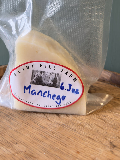 Wedge of Flint Hill Farm cow milk Manchego, vacuum sealed, on a wooden barrel