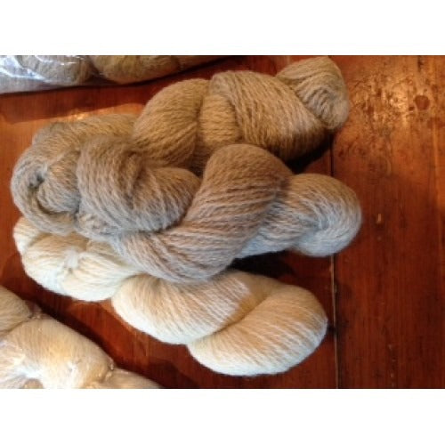 Madejas de hilo de lana hilado a mano y sin teñir, en crema, gris plata y beige, sobre una mesa de madera