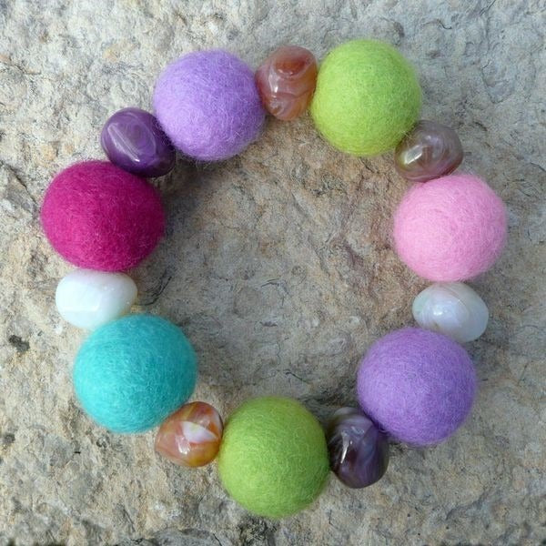 Una pulsera elástica de cuentas de lana afieltrada a mano en magenta, lila, verde limón, turquesa y rosa, alternadas con ágata pulida