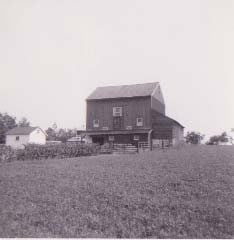 Archival photograph of the bank barn seen across a plowed field