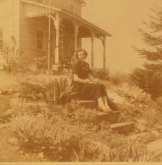 A woman sitting on the steps of the farmhouse porch among the garden plantings, sepia archival photograph