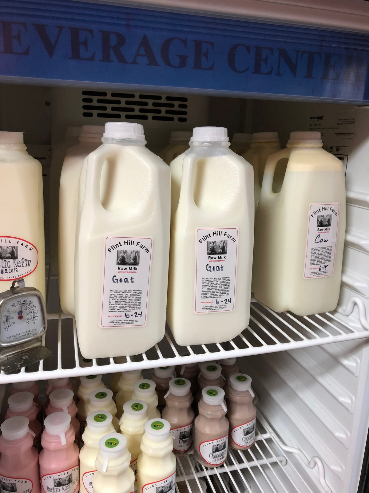 Farm store refrigerator case stocked with Flint Hill Farm half-gallon jugs of raw cow and goat milk, chocolate milk and kefir below
