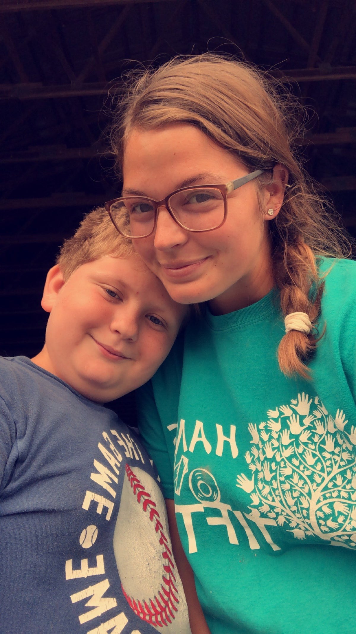 Selfie of two people leaning head to head in a dim barn, a young adult in a teal charity T-shirt and a young child in a blue T-shirt, both smiling