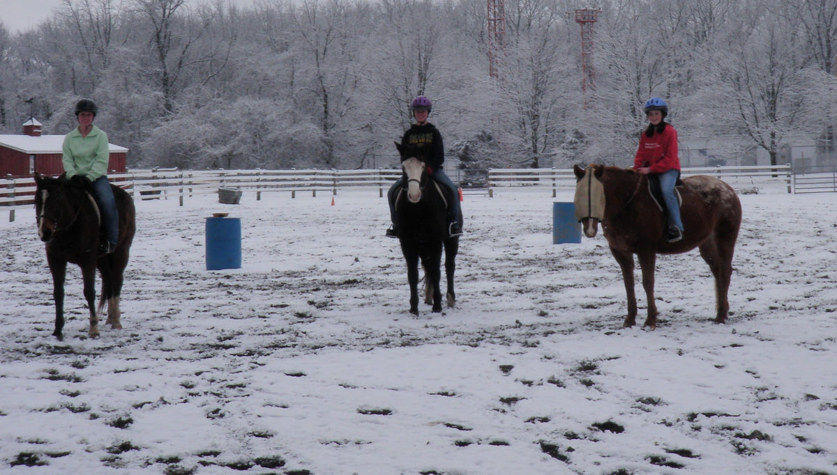 Three helmeted riders lined up on horseback in the snowy outdoor riding ring
