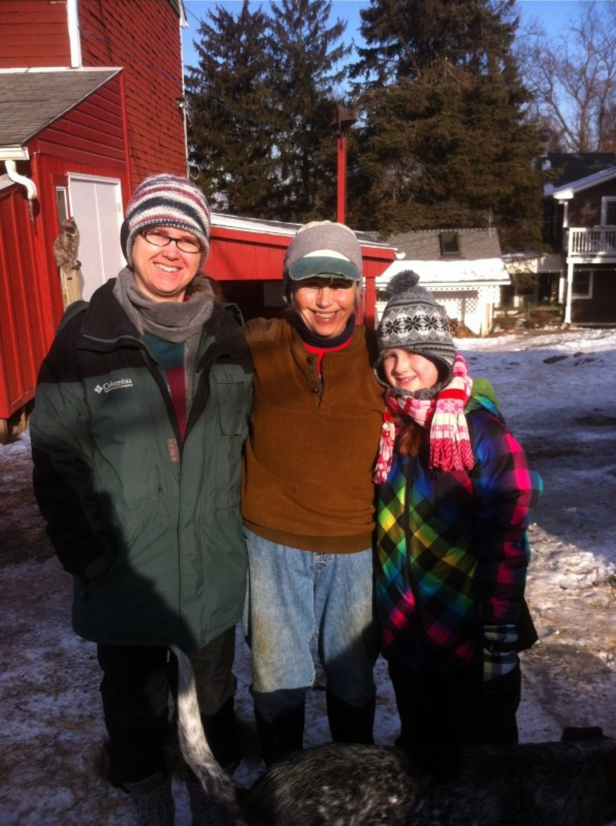 Kathy with two guests bundled up in winter, standing in front of a red barn