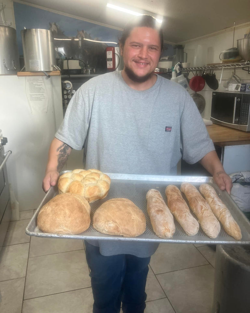 A baker holding a tray of fresh-baked bread and rolls in the farm kitchen